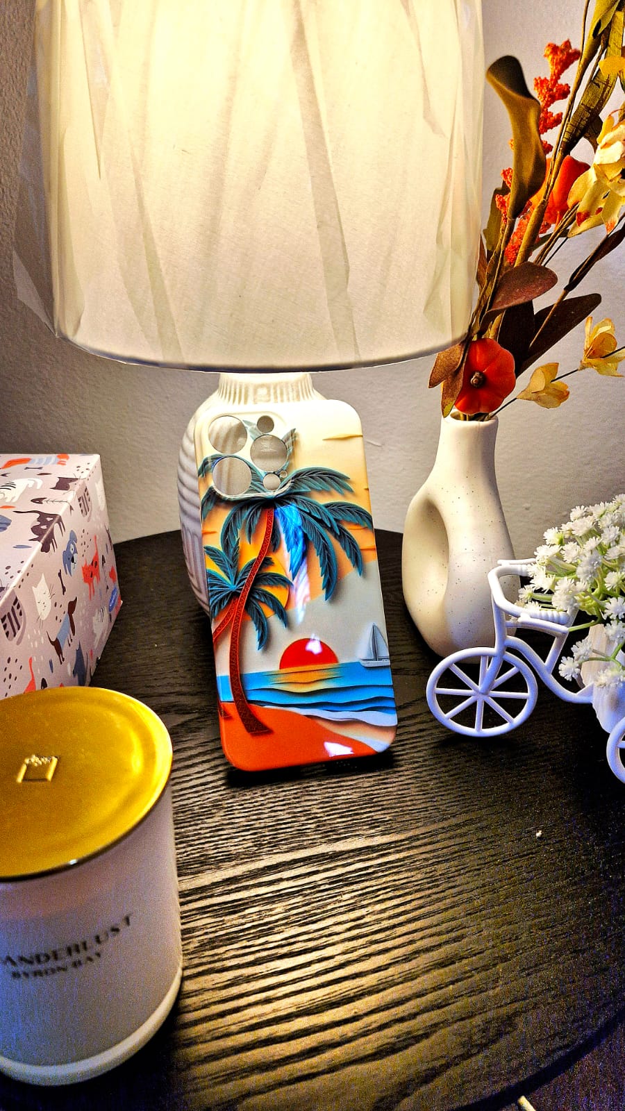 Sunset palm tree phone case styled on dark wood table with lamp